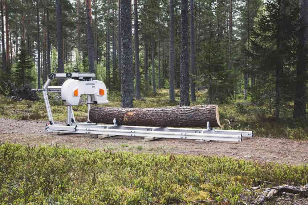 A Logosol B701 band sawmill in a pine forest, with a pine log on the aluminum bed.
